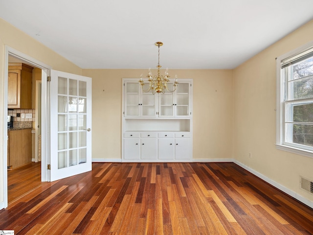 unfurnished dining area with dark wood-type flooring, a healthy amount of sunlight, and a notable chandelier