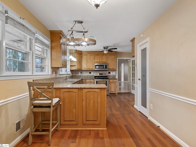 kitchen featuring sink, hanging light fixtures, kitchen peninsula, decorative backsplash, and appliances with stainless steel finishes