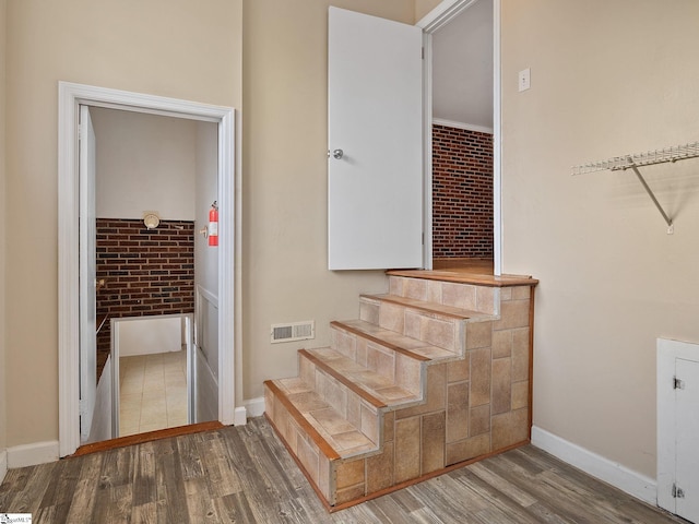 stairs featuring hardwood / wood-style floors, ornamental molding, and brick wall