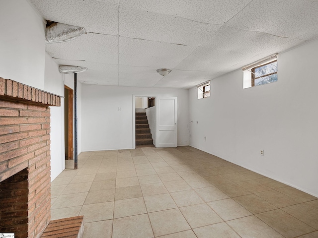 basement with a drop ceiling, light tile patterned flooring, and a brick fireplace