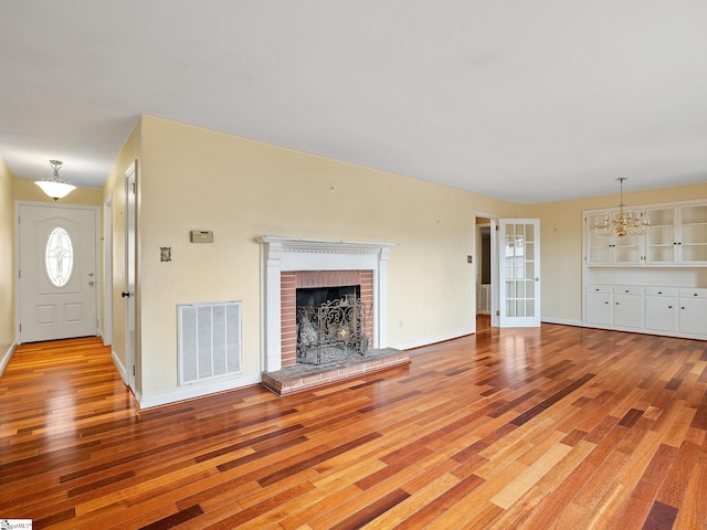 unfurnished living room with a brick fireplace, light hardwood / wood-style floors, and a notable chandelier