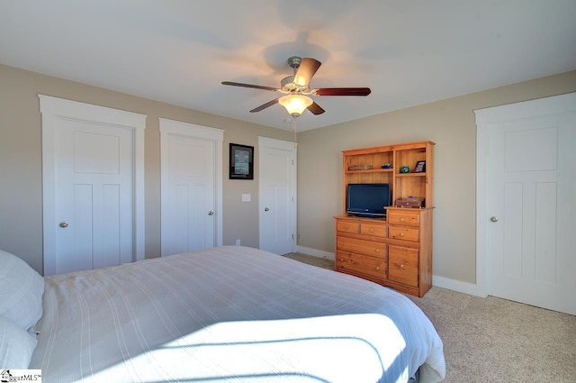 bedroom featuring two closets, light colored carpet, and ceiling fan