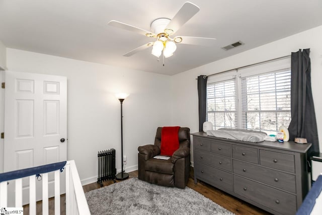 bedroom with ceiling fan, dark hardwood / wood-style flooring, and a crib