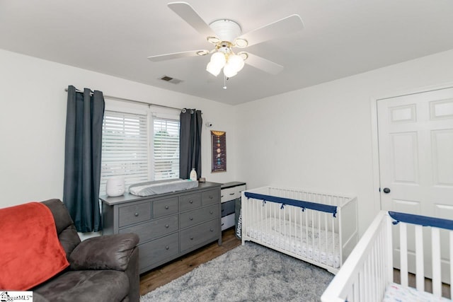 bedroom with hardwood / wood-style floors, ceiling fan, and a nursery area