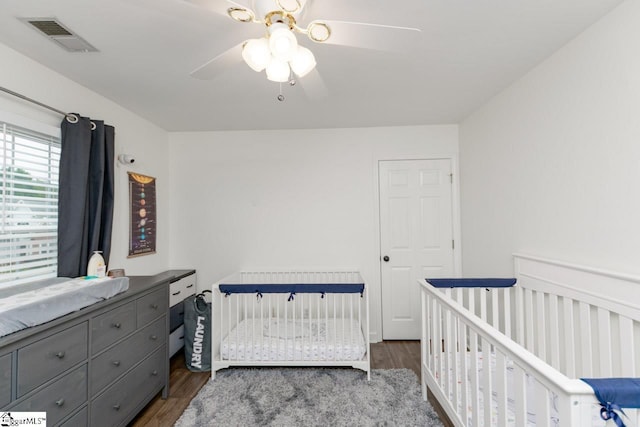 bedroom featuring ceiling fan, dark hardwood / wood-style flooring, and a crib