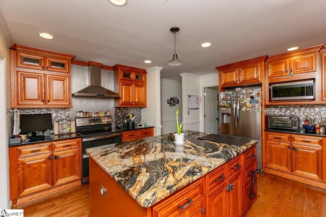 kitchen featuring appliances with stainless steel finishes, dark stone counters, wall chimney exhaust hood, decorative light fixtures, and a kitchen island