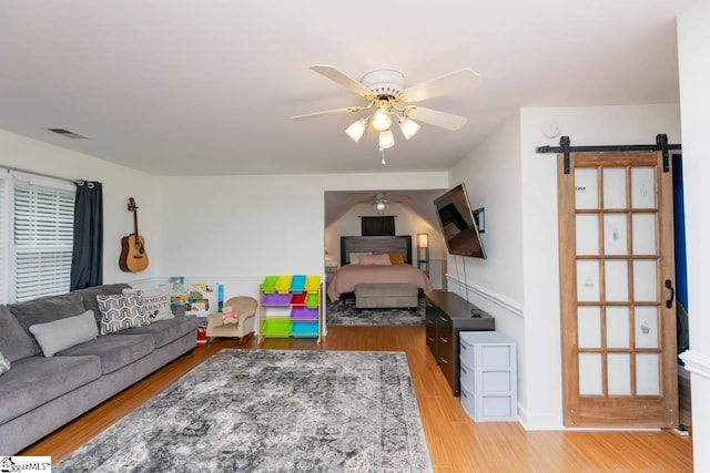 living room featuring light wood-type flooring, a barn door, and ceiling fan