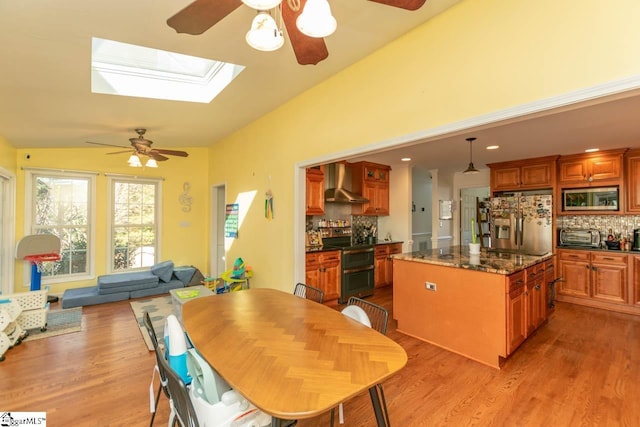 dining area featuring light hardwood / wood-style flooring, ceiling fan, and vaulted ceiling with skylight