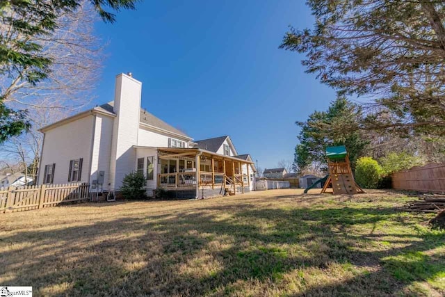 rear view of house with a playground, a sunroom, and a lawn