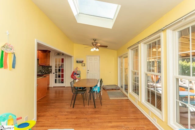 dining room featuring ceiling fan, lofted ceiling with skylight, and light hardwood / wood-style flooring