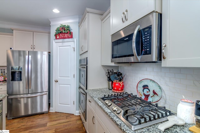 kitchen featuring tasteful backsplash, light stone counters, appliances with stainless steel finishes, white cabinets, and hardwood / wood-style flooring