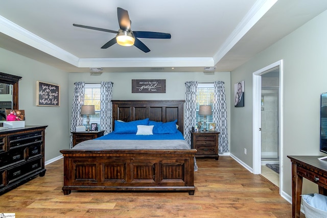 bedroom featuring ensuite bathroom, ceiling fan, ornamental molding, a tray ceiling, and light hardwood / wood-style floors