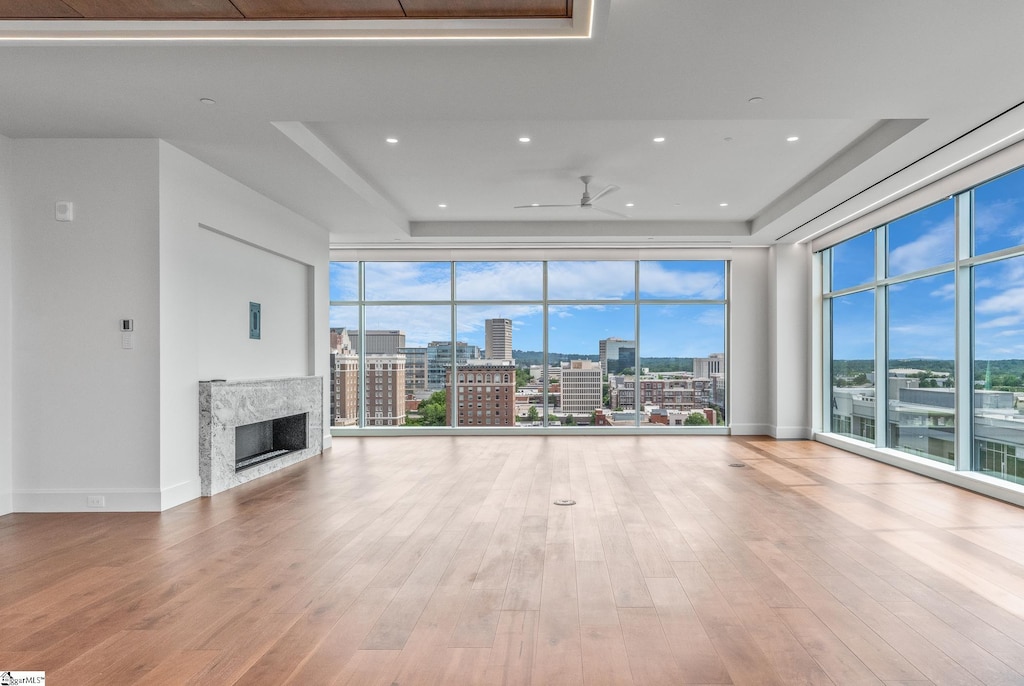 unfurnished living room with wood-type flooring, ceiling fan, a high end fireplace, a wealth of natural light, and a tray ceiling