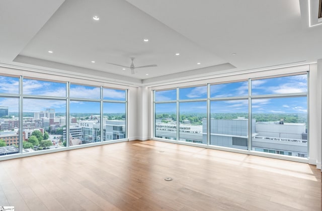 interior space with wood-type flooring, expansive windows, a raised ceiling, and ceiling fan