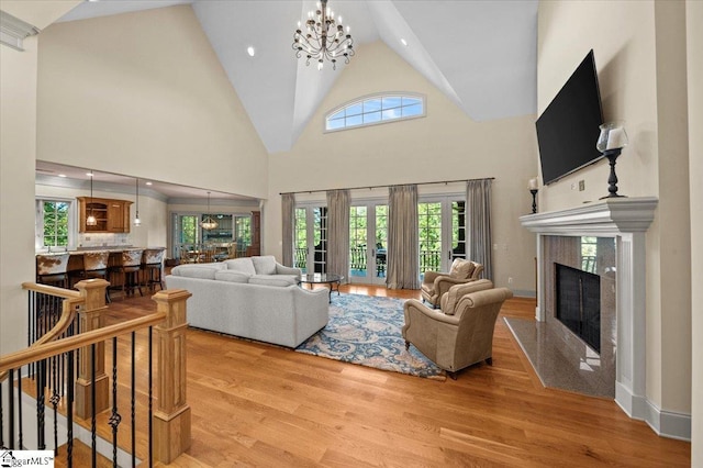 living room with a high end fireplace, an inviting chandelier, light hardwood / wood-style floors, and high vaulted ceiling