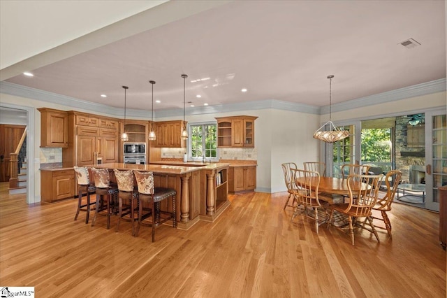 kitchen featuring backsplash, decorative light fixtures, an inviting chandelier, light hardwood / wood-style flooring, and a large island