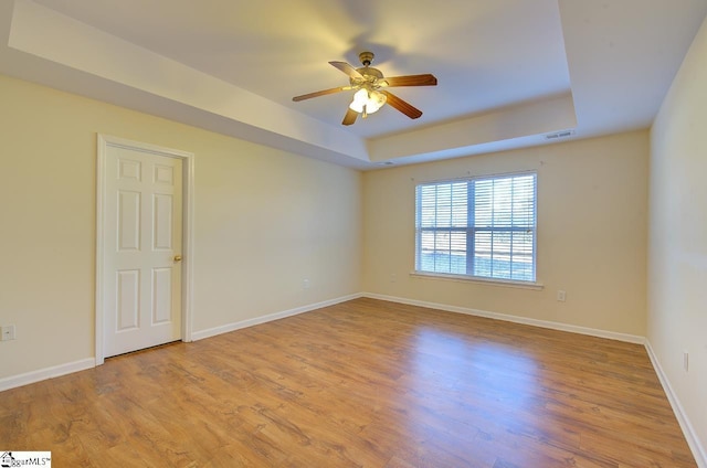 unfurnished room with a raised ceiling, ceiling fan, and light hardwood / wood-style floors