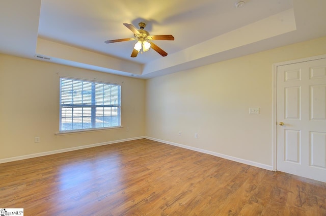 empty room featuring a tray ceiling, ceiling fan, and light hardwood / wood-style floors