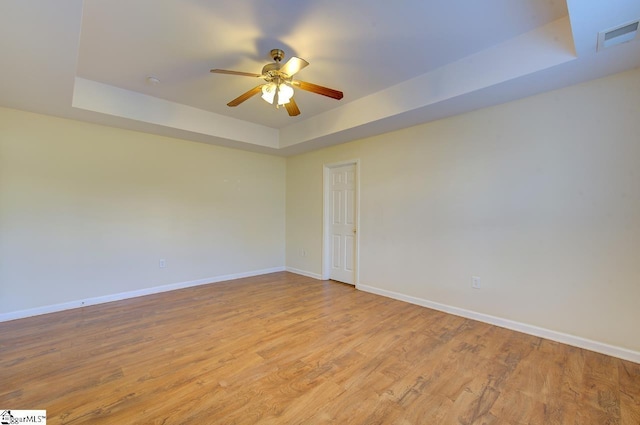 spare room featuring ceiling fan, a raised ceiling, and light wood-type flooring