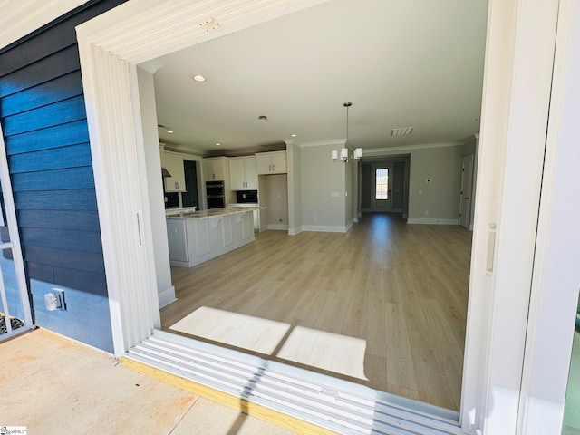 interior space with crown molding, decorative light fixtures, light hardwood / wood-style flooring, a chandelier, and white cabinetry