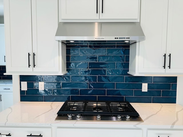 kitchen with tasteful backsplash, black gas stovetop, wall chimney exhaust hood, and light stone countertops