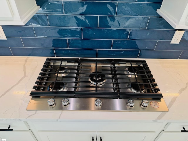 interior details with light stone countertops, white cabinets, and black gas stovetop