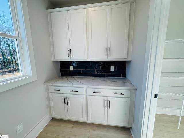 bar featuring backsplash, white cabinetry, light stone countertops, and light wood-type flooring