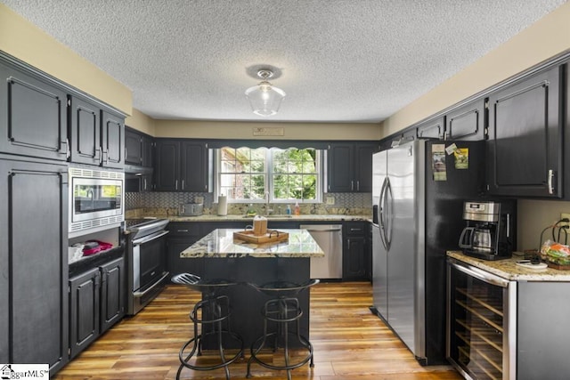 kitchen with decorative backsplash, a kitchen island, light stone counters, stainless steel appliances, and beverage cooler