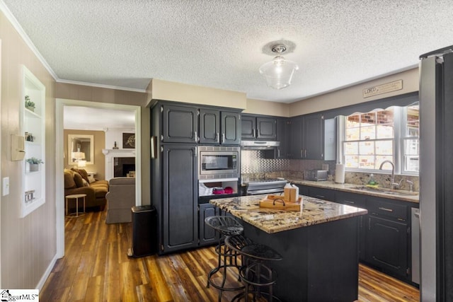 kitchen with light stone countertops, sink, dark wood-type flooring, a kitchen island, and appliances with stainless steel finishes