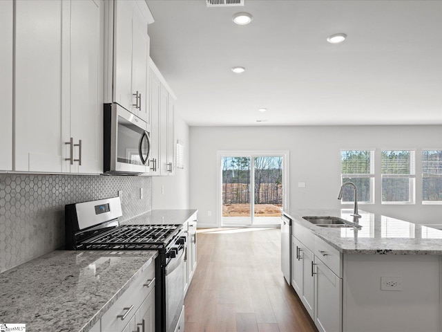 kitchen featuring stainless steel appliances, tasteful backsplash, white cabinetry, a sink, and wood finished floors