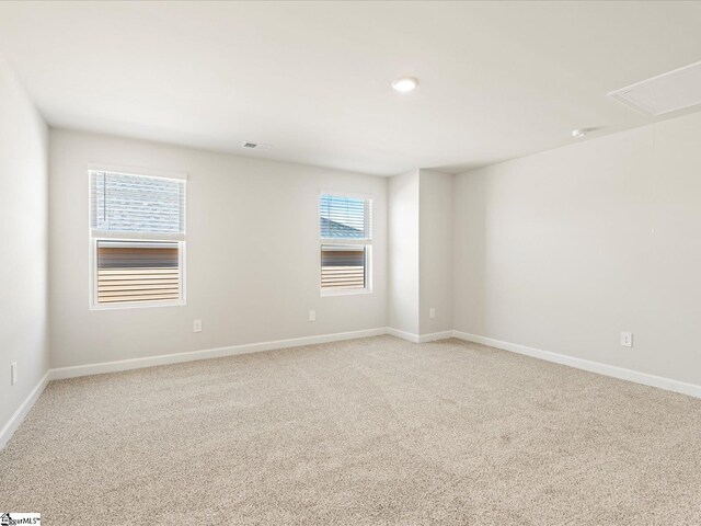 empty room featuring attic access, light carpet, visible vents, and baseboards