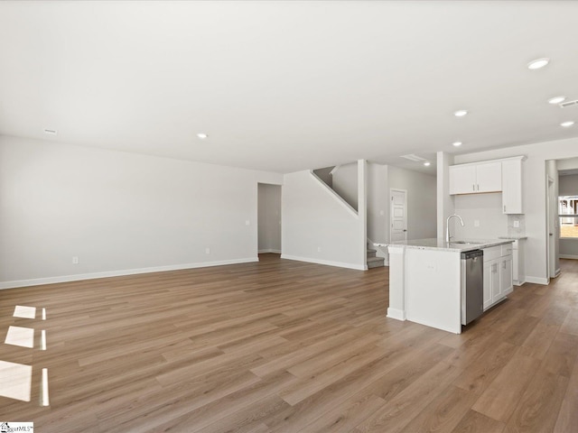 kitchen featuring light wood finished floors, white cabinets, a sink, dishwasher, and baseboards