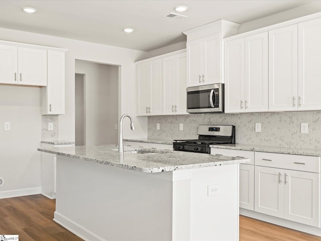 kitchen with visible vents, white cabinets, a kitchen island with sink, stainless steel appliances, and a sink