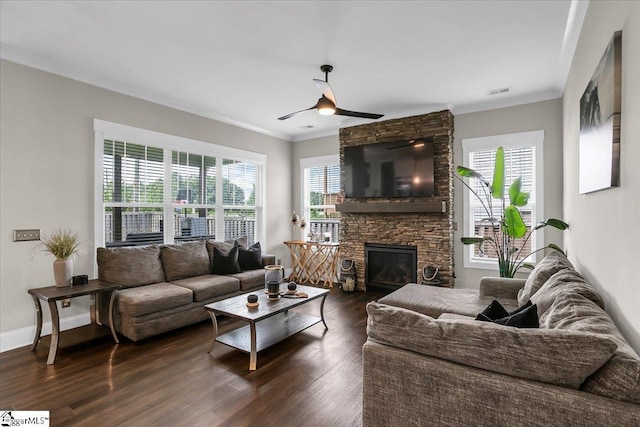 living room with ceiling fan, a stone fireplace, dark wood-type flooring, and crown molding