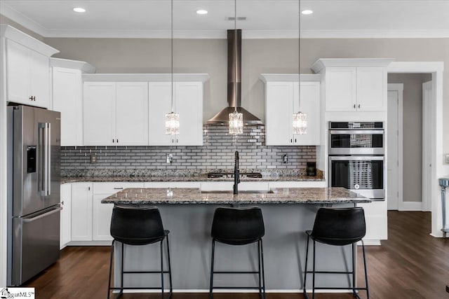 kitchen featuring pendant lighting, wall chimney exhaust hood, a kitchen island with sink, and appliances with stainless steel finishes