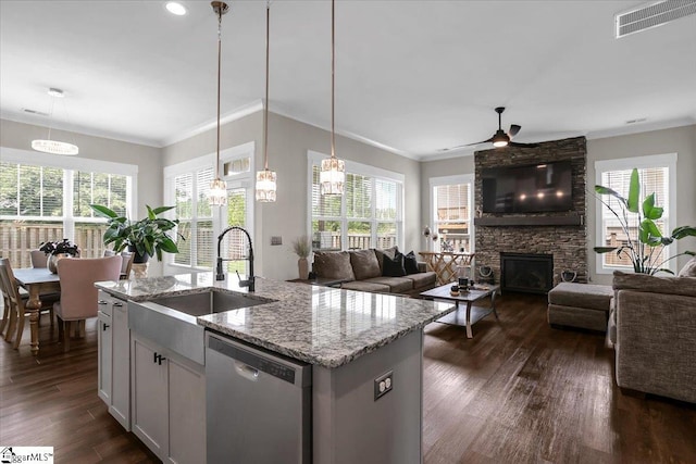 kitchen with light stone counters, sink, pendant lighting, dishwasher, and an island with sink