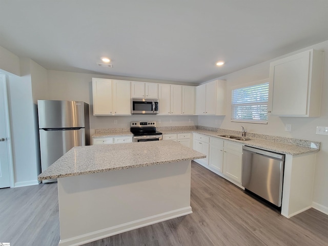 kitchen featuring light stone countertops, stainless steel appliances, sink, white cabinetry, and a kitchen island