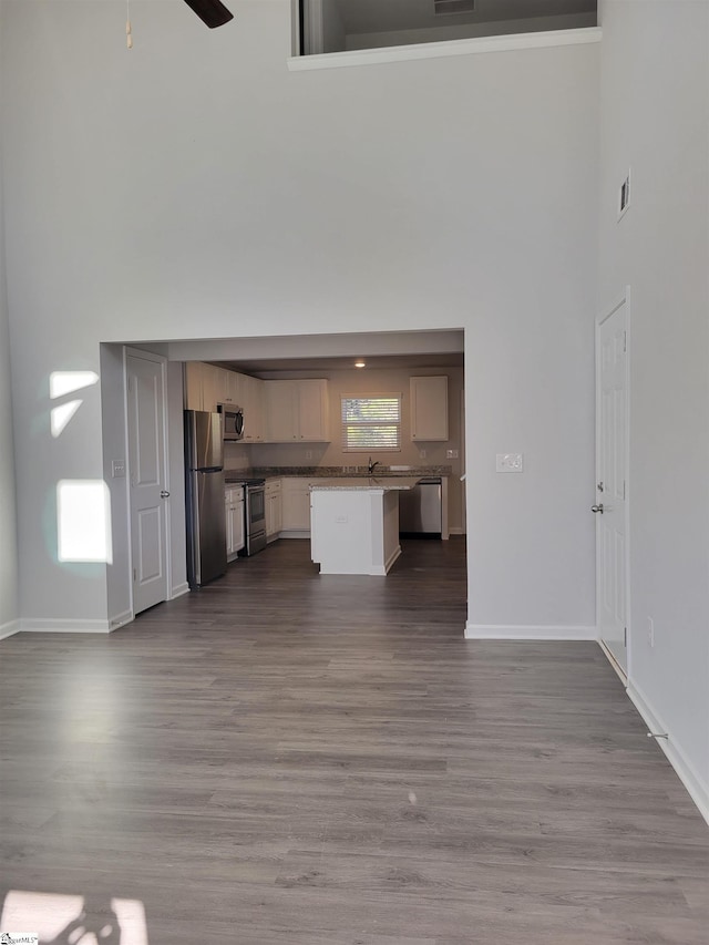 unfurnished living room with ceiling fan, wood-type flooring, and a towering ceiling