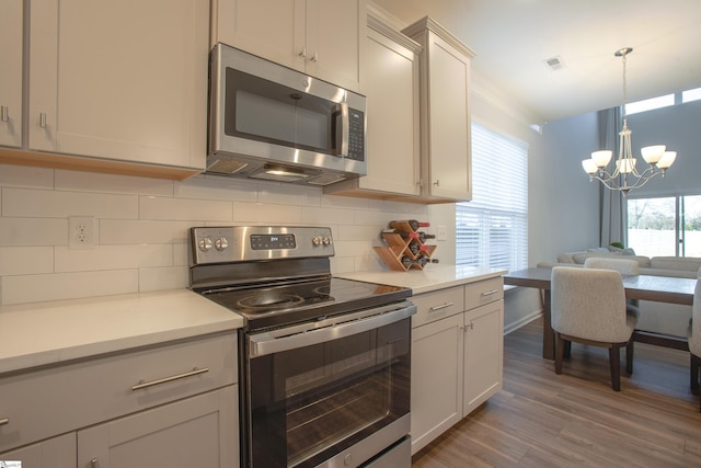 kitchen with hardwood / wood-style floors, backsplash, hanging light fixtures, a notable chandelier, and stainless steel appliances