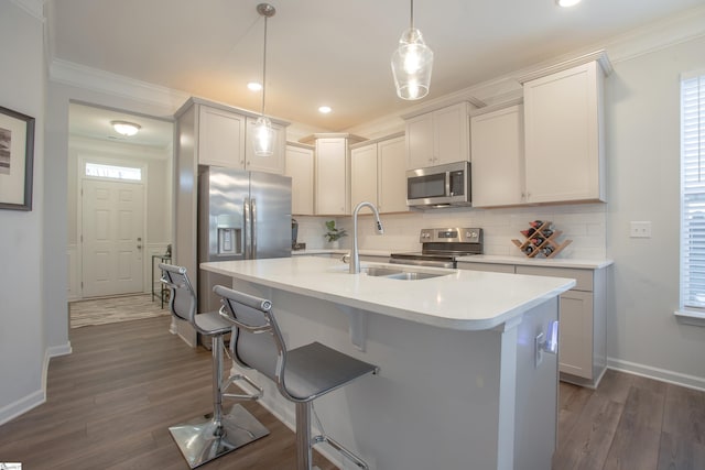 kitchen featuring stainless steel appliances, sink, decorative light fixtures, dark hardwood / wood-style floors, and an island with sink