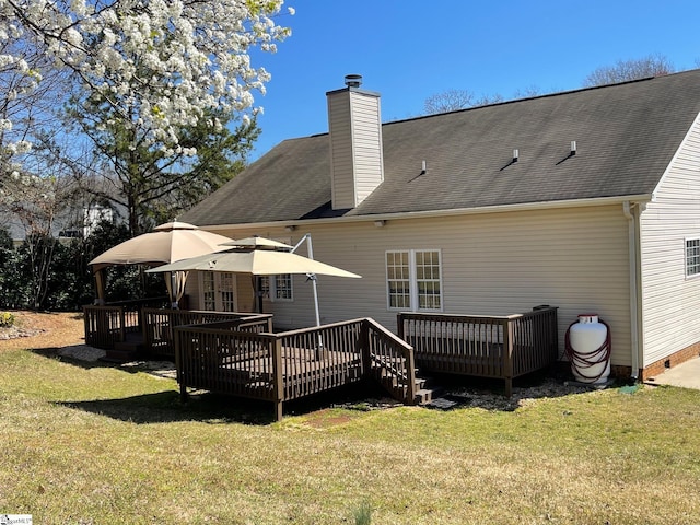 rear view of property with a shingled roof, a wooden deck, a yard, and a chimney