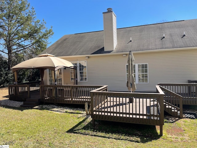 back of property with a deck, a lawn, a shingled roof, and a chimney