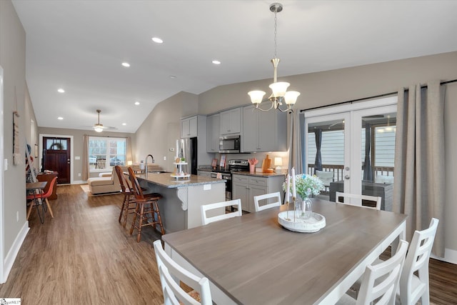 dining area with french doors, light wood-type flooring, ceiling fan with notable chandelier, vaulted ceiling, and sink