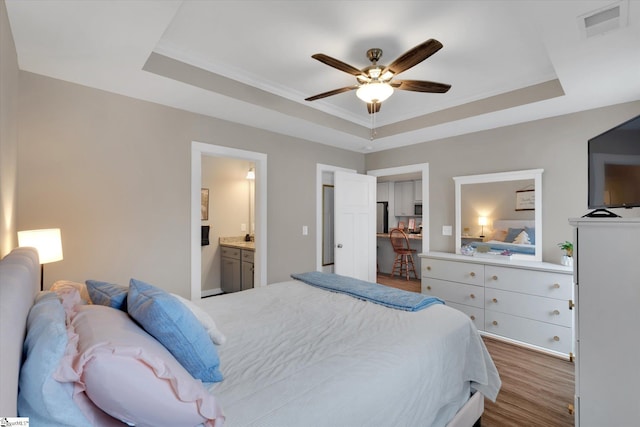 bedroom with ensuite bathroom, ceiling fan, and a raised ceiling