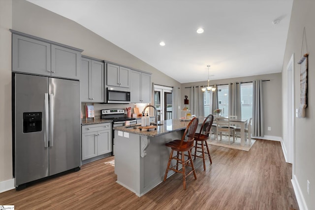 kitchen featuring stainless steel appliances, sink, dark stone countertops, gray cabinets, and an island with sink