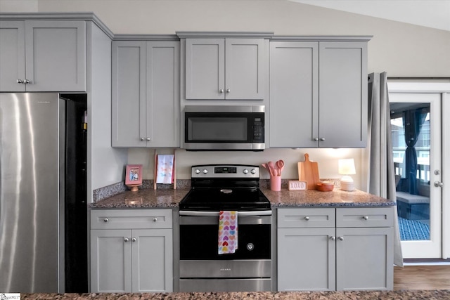 kitchen featuring dark stone countertops, gray cabinets, lofted ceiling, and appliances with stainless steel finishes