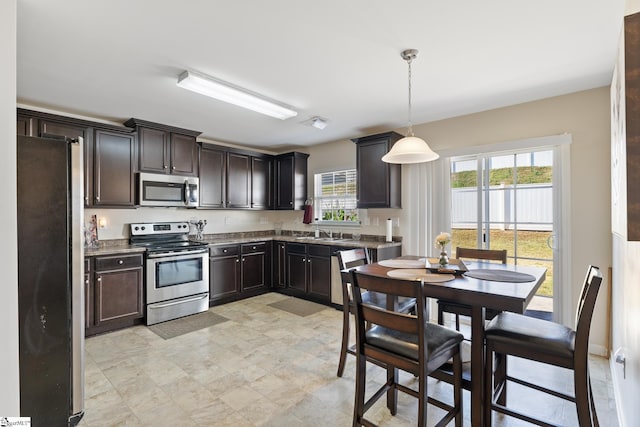 kitchen featuring a wealth of natural light, pendant lighting, stainless steel appliances, and dark brown cabinets