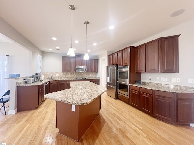 kitchen with kitchen peninsula, appliances with stainless steel finishes, a center island, light hardwood / wood-style floors, and hanging light fixtures