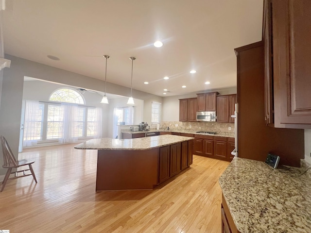 kitchen featuring a center island, stainless steel appliances, hanging light fixtures, and light hardwood / wood-style floors