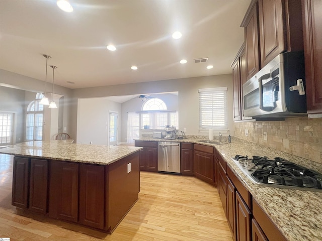 kitchen featuring decorative backsplash, appliances with stainless steel finishes, a center island, light hardwood / wood-style floors, and hanging light fixtures